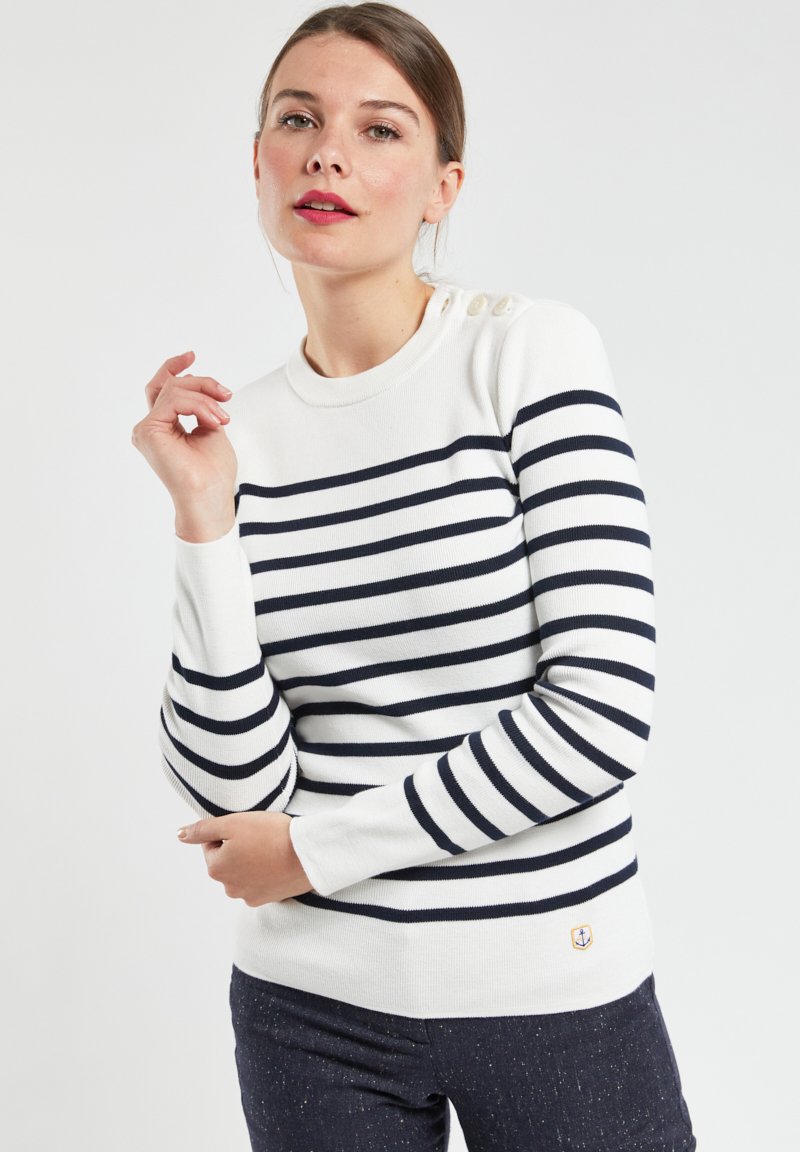 Pull rayé blanc et marine, avec un col rond, des manches longues et des accents en boutons sur l'épaule. Texture douce et design ajusté.