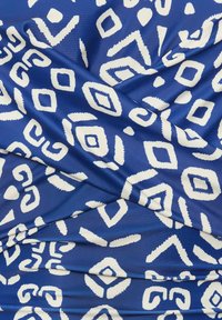 Tissu bleu avec des motifs géométriques blancs, y compris des diamants et des courbes. Texture lisse avec des sections froncées créant une profondeur visuelle.