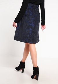 En mörkblå kjol med en texturerad tyg och subtilt mönster, ihop med svarta mockakängor med grov klack.