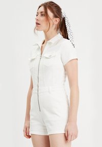 Weißer Denim-Overall mit Kragen, kurzen Ärmeln und einem Reißverschluss vorne. Verfügt über zwei Brusttaschen und eine figurbetonte Silhouette. Glatte Textur.