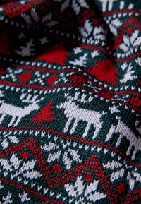 Adīšanas audums ar atkārtotu balto ziemeļbriežu, sarkano koku un ģeometrisku dizainu rakstu uz tumši zaļa fona. Strukturēta apdare.