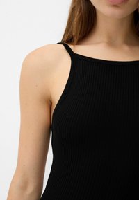 Black ribbed tank top with thin straps, featuring a fitted design and textured fabric. The neckline is slightly scooped.