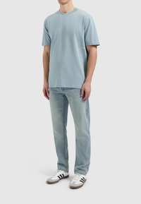 Lichtblauwe katoenen T-shirt met een ronde hals en korte mouwen, gedragen met lichtblauwe denim jeans en witte sneakers met zwarte strepen.