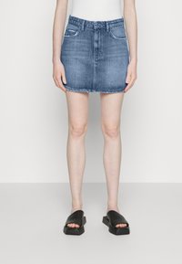 Saia mini de ganga na cor azul clara com um design ajustado, cinco bolsos e bainha desfiada. Combinada com sandálias pretas de slide, com bico quadrado.