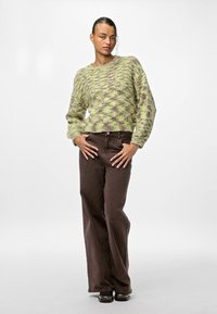 Grüner und lila gestrickter Pullover mit langen Ärmeln, kombiniert mit braunen weit geschnittenen Hosen. Das Outfit wird durch schwarze Schuhe ergänzt.
