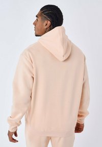 Hoodie in zacht perzikstof, met een ontspannen pasvorm en ribgebreide manchetten en onderrand. Glad textuur zonder zichtbare patronen of accenten.