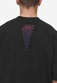 Black t-shirt featuring a stylized graphic on the back in gradient shades of pink and purple, arranged in a repeating pattern.