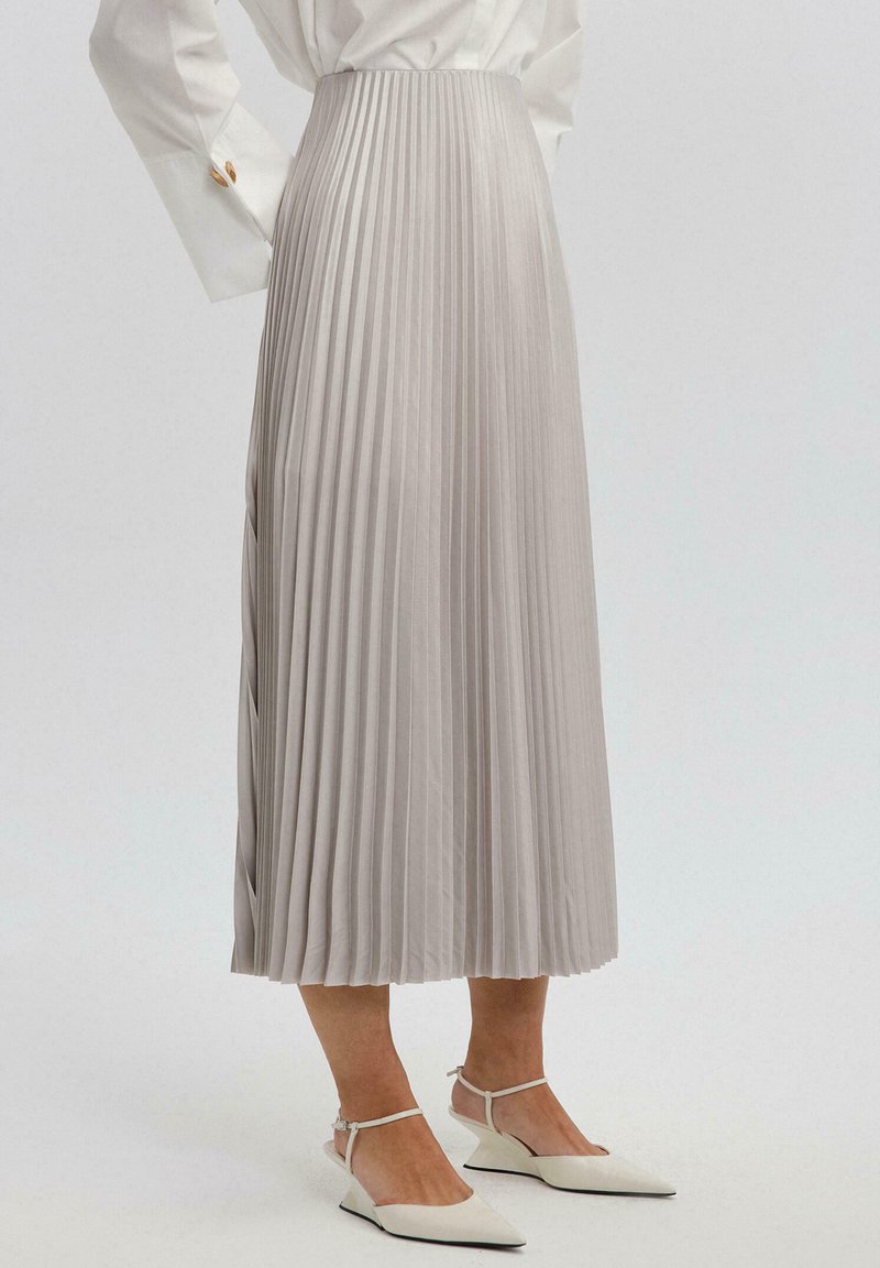 Hame midi pleated dalam kain abu-abu muda dengan tekstur halus, dilengkapi pinggang tinggi dan belahan samping untuk kemudahan bergerak.