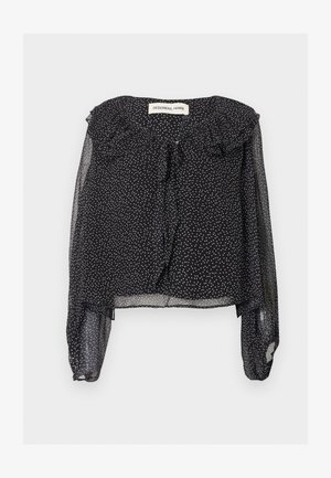 Bluză neagră transparentă cu buline albe, mâneci lungi bufante, guler volănat și panglică la decolteu, afișată așezată pe fundal alb.