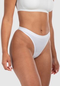 String en blanc en tissu lisse, avec une coupe basse, des bandes élastiques douces et une couverture minimale sur les côtés.