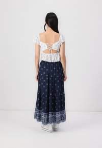 Fustă maxi fluidă, de culoare bleumarin, cu imprimeu floral. Top alb, cu mâneci scurte, cu decolteu la spate și detalii legate cu șiret. Adidași albi completează ținuta.