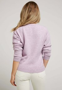 Pull lilas avec une texture, col rond et poignets côtelés, porté sur un pantalon blanc. Présente une coupe légèrement ample.