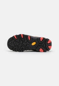 Svart gummisåle med aggressivt mønster og røde detaljer; har en gul Vibram-logo. Egnet for røft terreng.