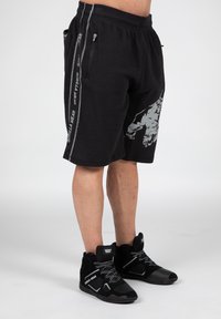 Zwarte mesh shorts met zijrits zakken, voorzien van een grafisch ontwerp en "GORILLA WEAR" branding. Gecombineerd met zwarte sportschoenen.