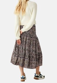 Gonna lunga a balze con stampa leopardata, caratterizzata da una vita arricciata. Il modello indossa un maglione color crema e sneakers sportive con un accento blu.