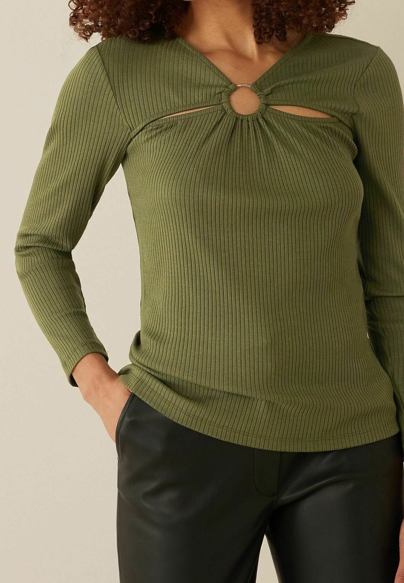Groene geribbelde longsleeve top met een V-hals, een centrale uitsnijding met een metalen ring en een aansluitend ontwerp, gecombineerd met zwarte leren broek.