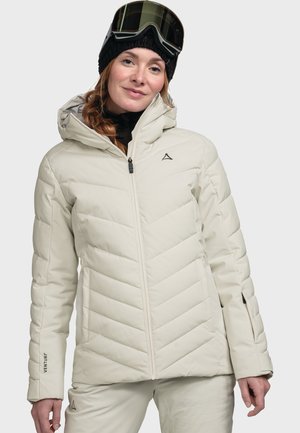 Hellbeige isolierte Jacke mit Zickzackmuster, Reißverschluss und verstellbarem Kapuzenbereich. Besitzt ein Logo auf der Brust und ein Etikett an den Bündchen.
