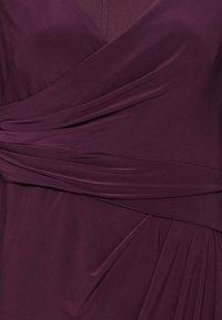 Viininpunainen mekko, jossa on kietaisumallinen muotoilu ja poimutetut yksityiskohdat, valmistettu sileästä, joustavasta kankaasta. V-pääntie ja kevyt laskostus.