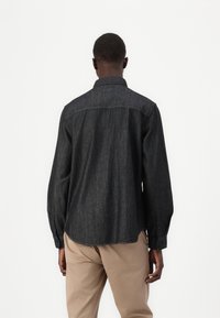 Dark denim shirt featuring a pointed collar, long sleeves with button cuffs, and a slightly curved hem. Textured fabric with subtle shading.