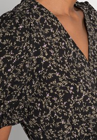 Robe noire à fleurs avec un décolleté plongeant en V, des manches bouffantes et un motif délicat de fleurs violettes et de feuilles vertes sur un tissu texturé.