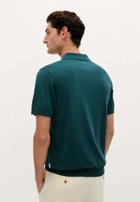 Grøn kortærmet polo shirt lavet af blødt stof, med klassisk krave, ribbede mansjetter og en let figursyet silhuet.