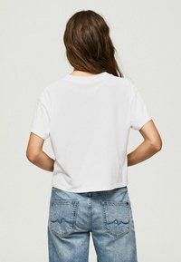 Camiseta blanca recortada de manga corta, hecha de una tela suave, combinada con unos jeans de tiro alto en azul claro que presentan un sutil bordado en los bolsillos.