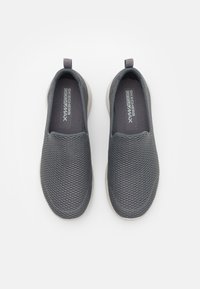 Baskets grises à enfiler avec une tige en maille, bout rond et semelle légère. Présente la marque "Skechers Goga Max" sur la semelle intérieure.
