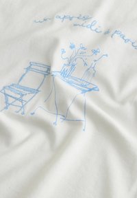 Țesătură albă cu broderie albastră reprezentând un scaun, o masă și o vază cu flori, având detalii decorative, creând un design minimalist.