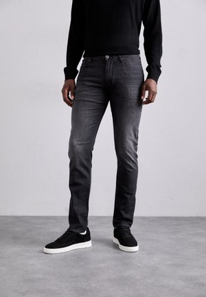 Kapeita slim-fit, tummanharmaat farkut, joissa on hienovaraisia kulumia, viiden taskun muotoilu ja hopeanvärinen nappi. Yhdistetty mustien mokkanahkaisten lenkkareiden kanssa.