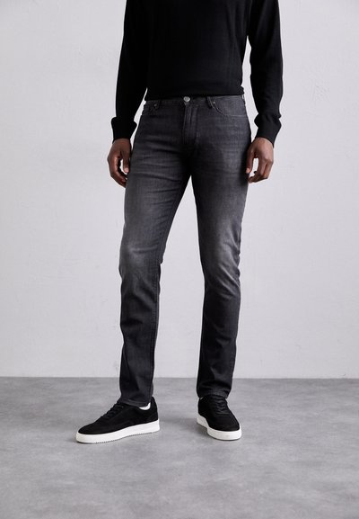 Jeans in denim grigio scuro slim-fit con leggero sbiadimento, design a cinque tasche e dettaglio in metallo argentato. Abbinati a sneakers in suede nere.