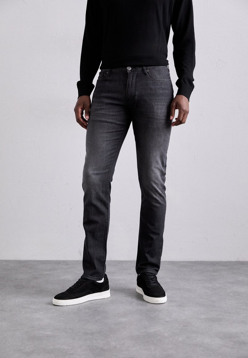 Uske slim-fit tamno sivi traperice s blagim izbljeđivanjem, pet džepova i detaljima od srebrnog dugmeta. Uparen s crnim nubuk tenisicama.