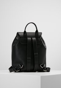 Czarny skórzany plecak o gładkiej fakturze, prostokątnym kształcie, górnym uchwycie i podwójnych paskach. Posiada metalowe okucia i subtelne zdobienia.
