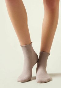 Beige ribbede korte sokker med en bølget kant, lavet af blødt stof. Designet til at sidde tæt om anklen, hvilket øger komforten.