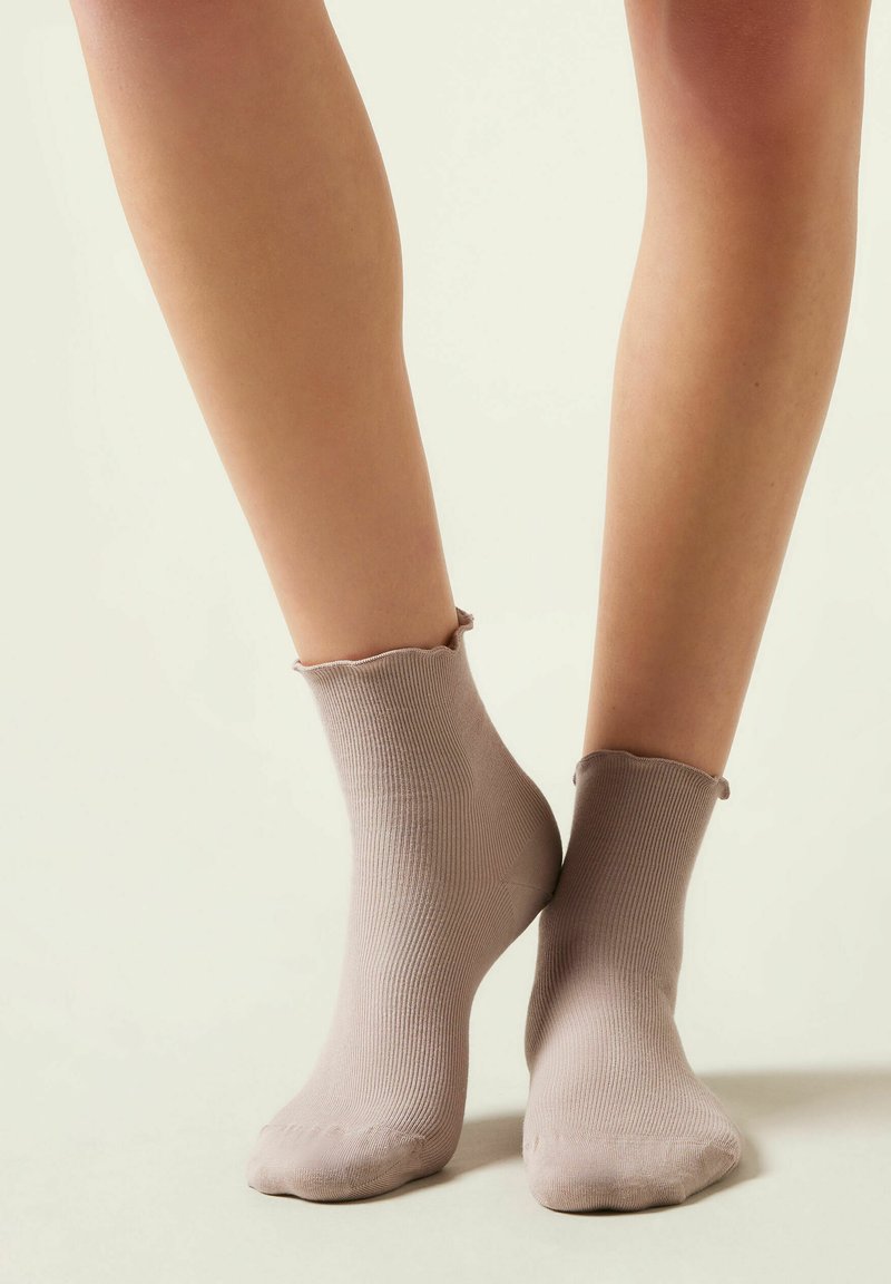 Calcetines cortos de canalé beige con un dobladillo ondulado, hechos de una tela suave. Diseñados para ajustarse cómodamente alrededor del tobillo, mejorando la comodidad.