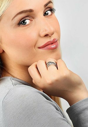 Silver ring with a textured band, worn on a hand with light skin; model has long, straight blonde hair and is wearing a gray top.
