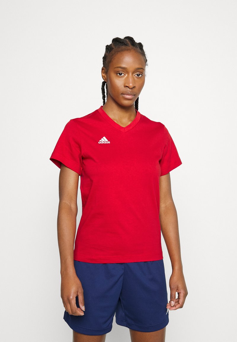 Červené bavlnené tričko s výstrihom do V a krátkymi rukávmi. Na ľavej strane hrude sa nachádza biele logo Adidas. Spárované s tmavomodrými šortkami.