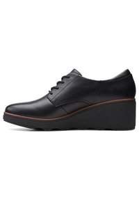 Chaussure compensée en cuir noir avec lacets à l’avant et bordure marron sur une semelle épaisse, vue du côté extérieur.