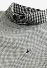Pull gris avec un tissu texturé et un col présentant un motif vichy noir et blanc. Petit logo noir à l'avant.