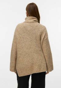 Suéter de punto beige con cuello alto, corte suelto y dobladillos acanalados. Tejido texturizado, suave, con sutiles variaciones de color en toda su superficie.