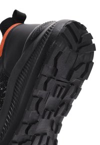 Baskets de sport noires avec semelle en caoutchouc texturé présentant des rainures profondes. Tige en matériau synthétique avec un accent orange et une languette de traction.