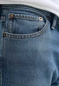 Ljust blå denimjeans med en texturerad yta, som har synlig sömnad, en liten ficka fram och metallaccenter.