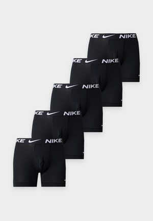 Päť čiernych Nike boxeriek s bielymi logopásikmi uložených diagonálne na bielom pozadí.