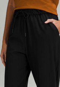 Czarne spodnie elastyczne w pasie z detalem sznurkowym, bocznymi kieszeniami i gładką fakturą. Materiał jest lekki i ma luźny krój.