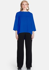 Blusa blu dal taglio morbido con scollatura rotonda e maniche a tre quarti, abbinata a pantaloni neri a gamba larga. Tessuto dalla texture liscia.