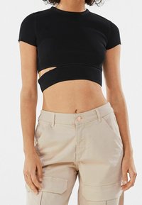 Svart randig croppad topp med korta ärmar och ett urklipp vid midjan, ihop med ljusbeige cargobyxor med knappstängning.