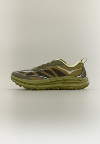 Παπούτσι για τρέξιμο σε μονοπάτια σε ελιά πράσινο χρώμα με παχιά σόλα, θηλιά στην φτέρνα και αντιολισθητική σόλα Vibram, εμφανιζόμενο σε πλευρική όψη σε ουδέτερο φόντο.