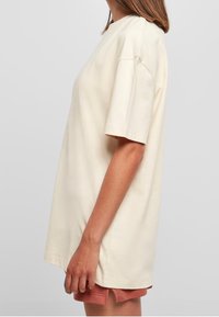 Krämfärgad bomull T-shirt, avslappnad passform, korta ärmar, rund halsringning, slät textur, höftlängd, stylad med ljusbruna shorts.