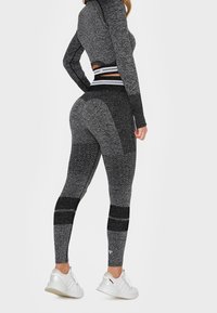 Šedé sportovní legíny s texturovanými vzory a černými akcenty, kombinované s odpovídajícím dlouhým rukávem a bílými sportovními botami.