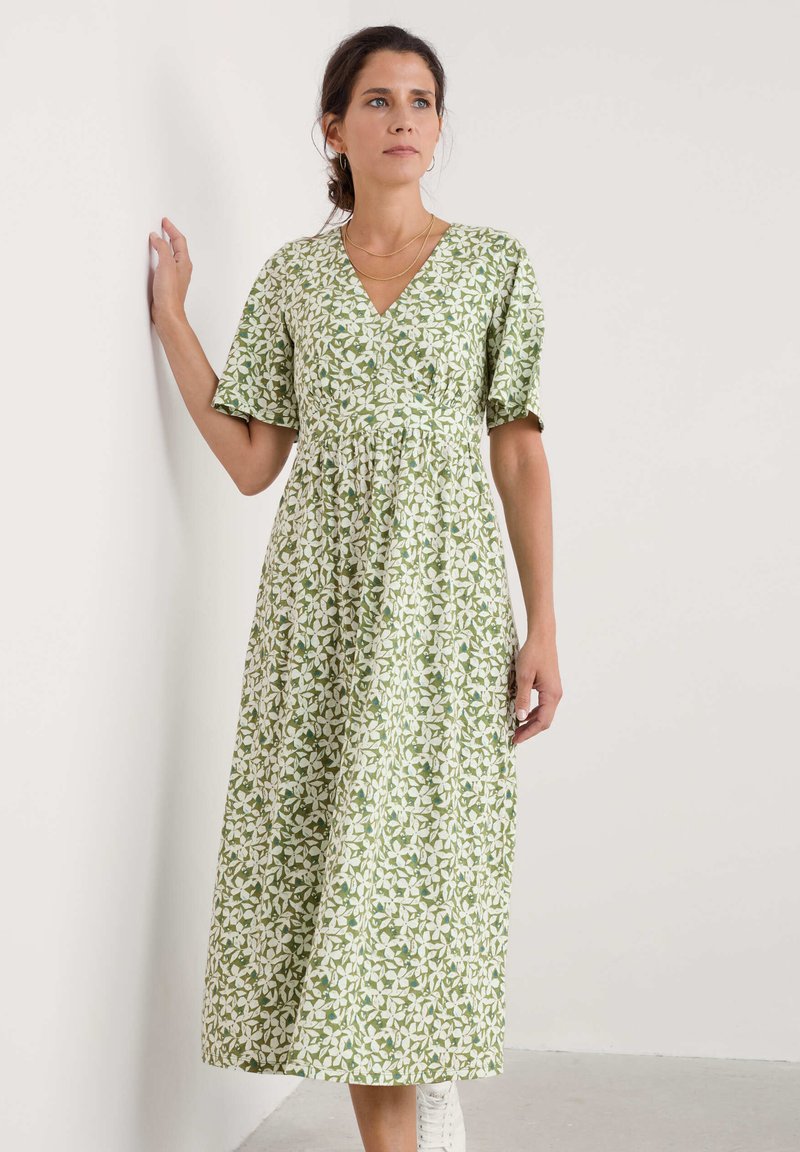 Vihreä kukkakuosiset mekko, jossa on lyhyet hihat, V-pääntie ja levenevä midipituinen hame. Yhdistettynä valkoisiin nilkkasaappaisiin, joissa on rento istuvuus.