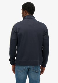 Marineblauwe sweatshirt met een hoge kraag, voorzien van een gladde textuur en contrasterende verticale strepen langs de schouders. Effen achterkant.